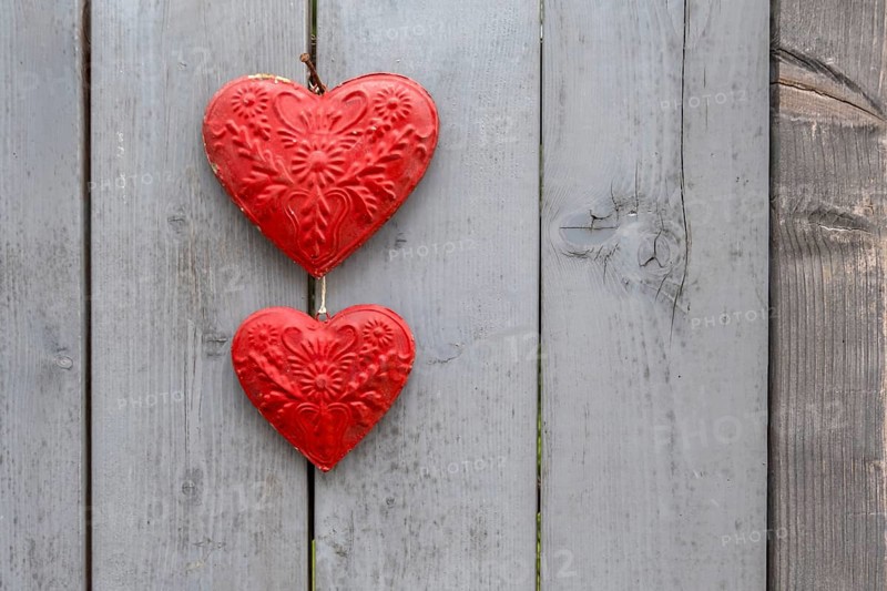 Two red metal hearts on a grey wooden gate