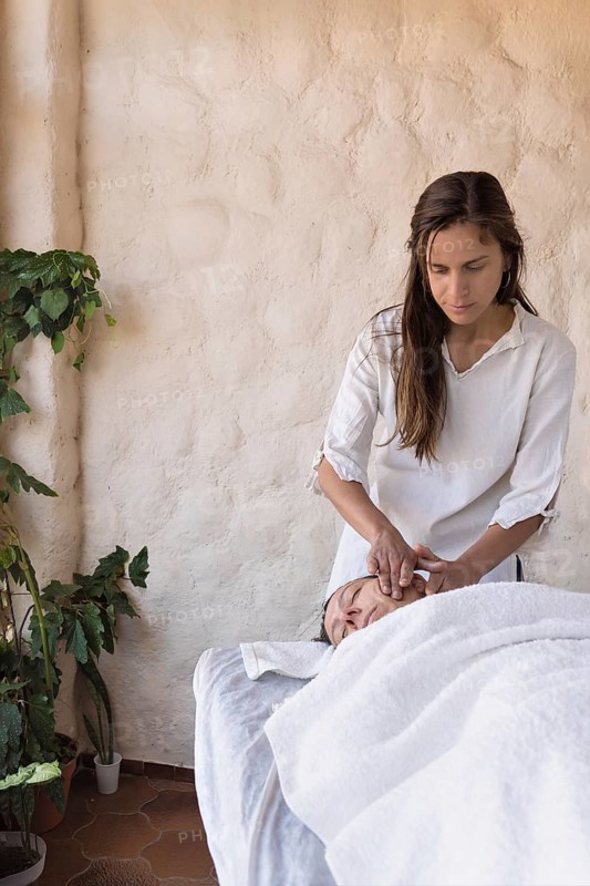 Young woman therapist and female patient having facial massage session massaging at beauty center