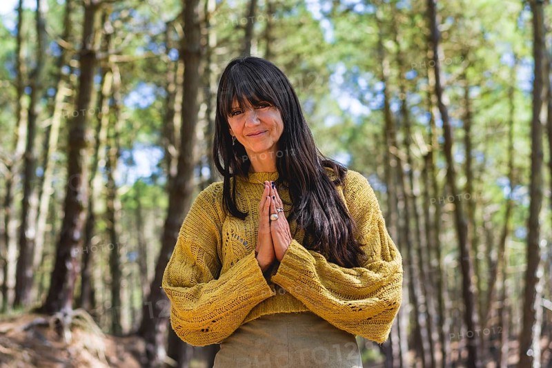 Smiling woman clasping hands while looking at camera outdoors