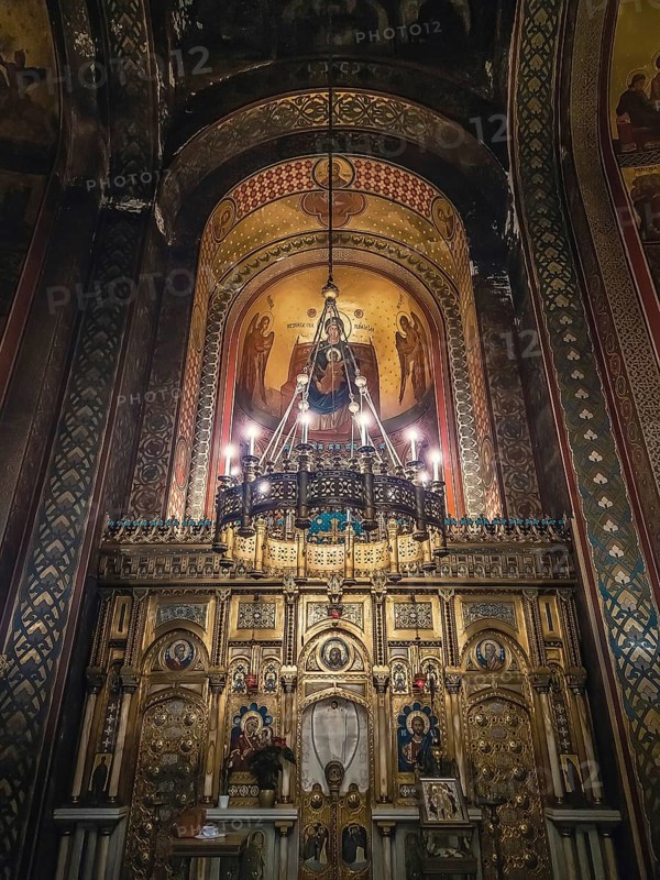 Interior details of Curtea de Arges monastery. The altar and ornate walls with painted icons and a golden chandelier with lights suspending out of ceiling