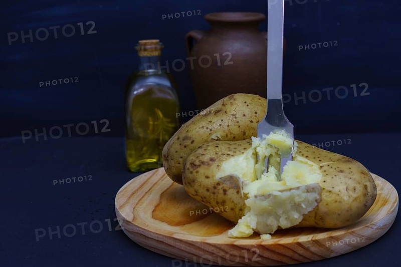 Boiled potato opened with a fork on a wooden plate