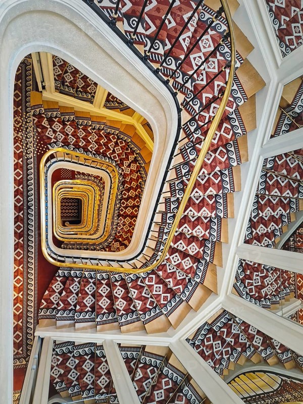 Abstract shape luxurious stairs with red carpet cover and golden handrail. Hypnotic pattern swirl staircase with mirror reflections on the stairwell walls