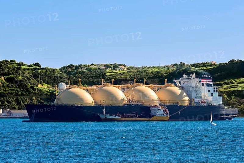 LNG or liquified natural gas tanker moored by industrial pier and green hill on sunny day. Alternative gas supply