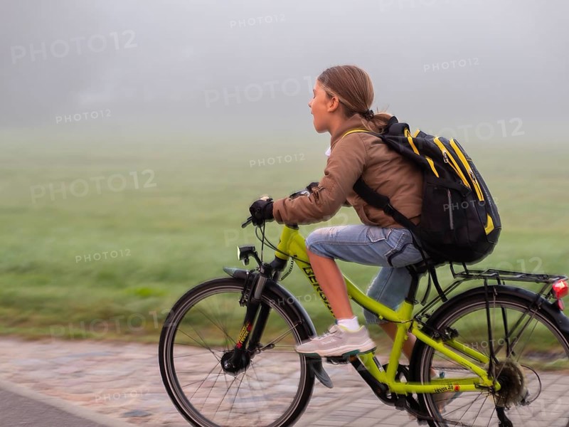 Boy with bicycle and schoolbag through the fog