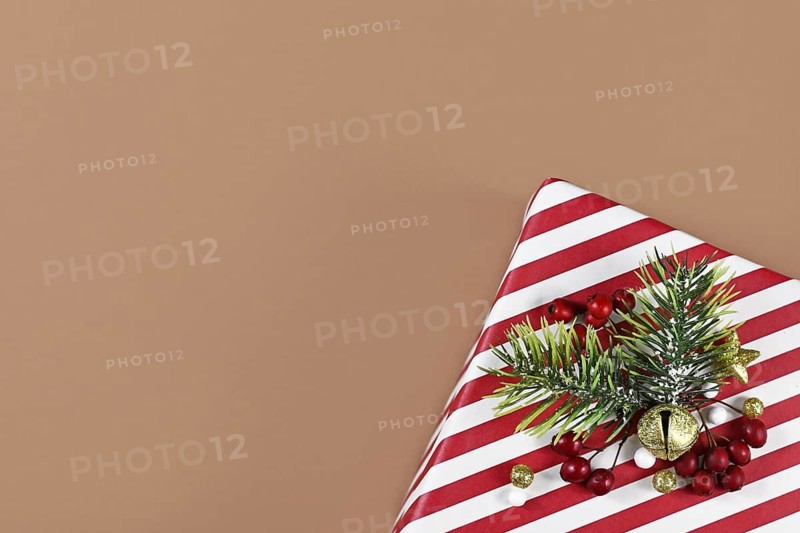Striped Christmas gift box with seasonal decoration in corner of brown background with empty copy space