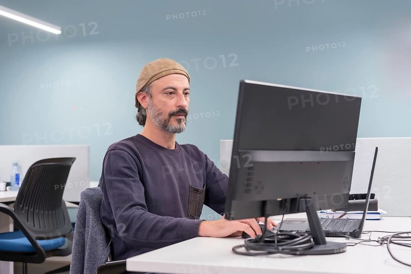 Portrait of a serious stylish mature man sitting on a desk using computer in a co-working
