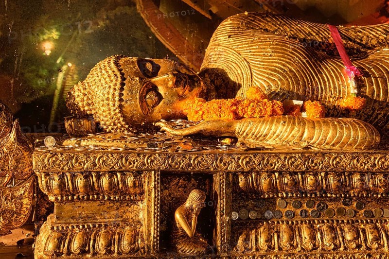 Statue of reclining Buddha covered with golden leaves