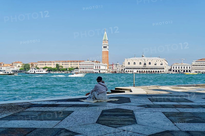Woman having a picnic in the square in front of the church of San Giorgio Maggiore on the Giudecca Canal with a view of the Doge's Palace
