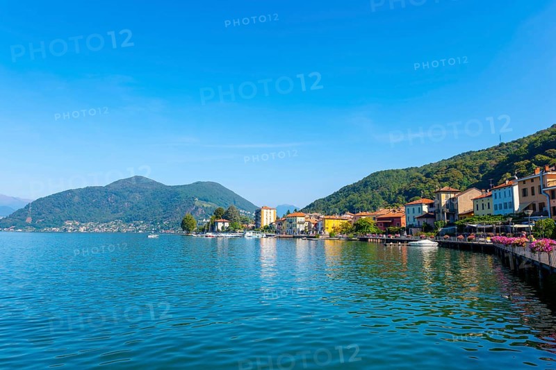 City of Porto Ceresio on Waterfront with Mountain and Lake Lugano in a Sunny Summer Day in Porto Ceresio