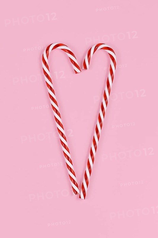 Christmas candy canes forming shape of heart on pink background