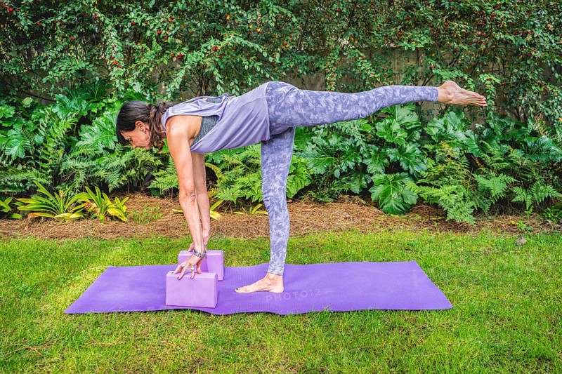 Fit woman in sportswear practices yoga pose using a block outdoors. Yoga with brick
