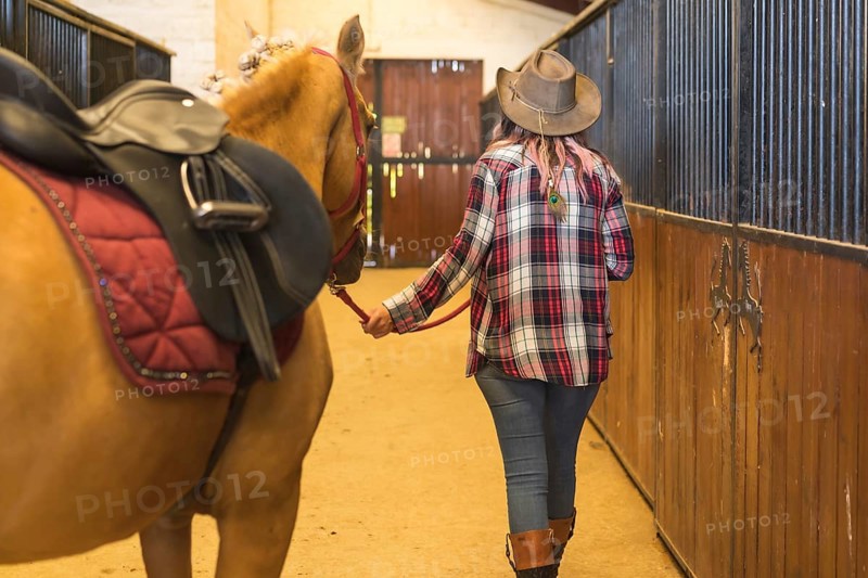 Unrecognizable cowgirl woman strolling with a horse in a stable