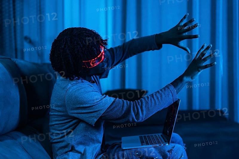 Afro man playing with laptop and Augmented reality goggles in a living room with neon blue light