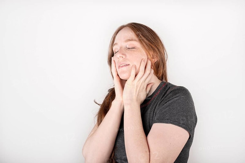 Beauty face. Smiling red haired woman touching healthy skin. Beautiful happy model with moisturized shiny fresh facial skin on white background in studio