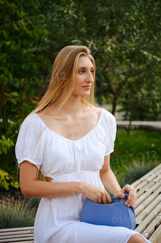 Young woman in white summer dress sitting on a bench waiting for someone
