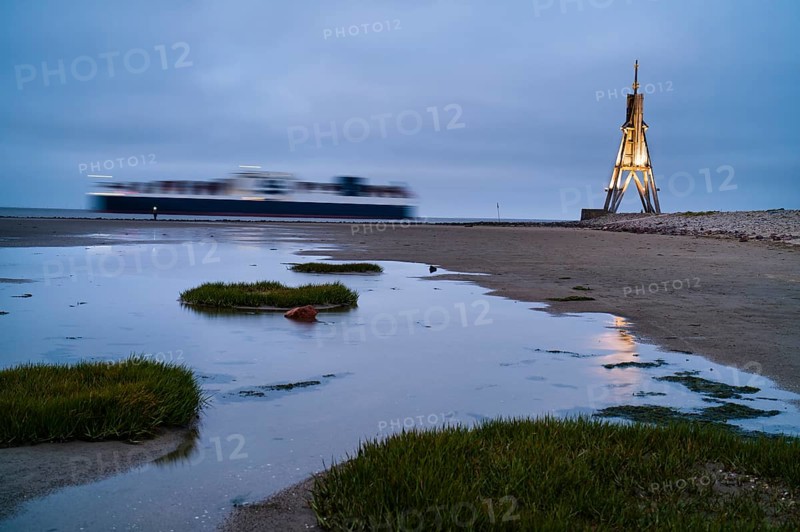 Kugelbake illuminated with cargo ship at dusk