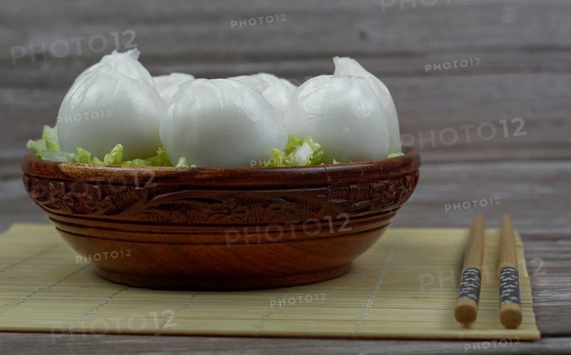 Xiao long bao of prawns on a bed of lettuce in a wooden bowl with chopsticks and a ceramic spoon with soy sauce