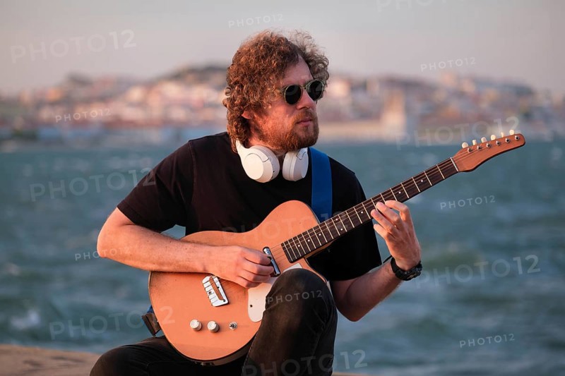 Hipster street musician in black playing electric guitar in the street on sunset on embankment