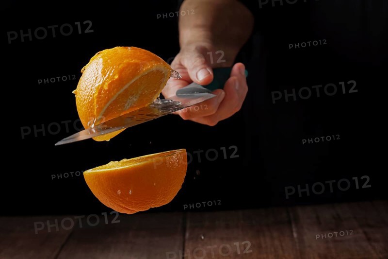 Woman cutting an orange in half with a knife in the air spilling water