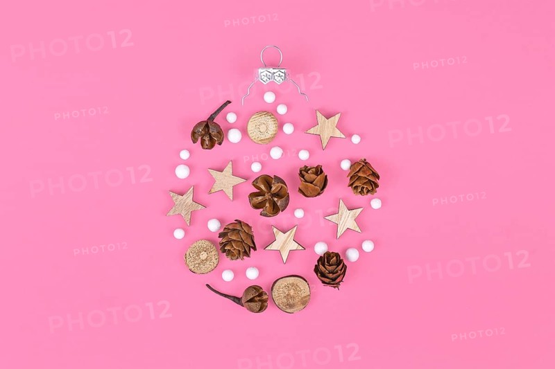 Seasonal ornaments like natural hernlock cones and stick slices with stars and white snowballs forming shape of Christmas tree bauble on pink background