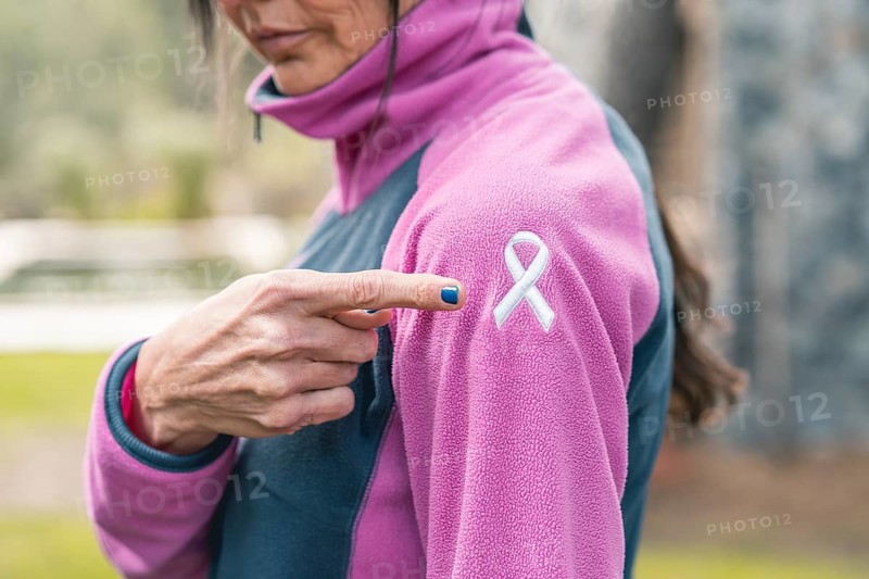 Mid adult woman pointing to an embroidered cancer awareness ribbon with her finger on her sweatshirt