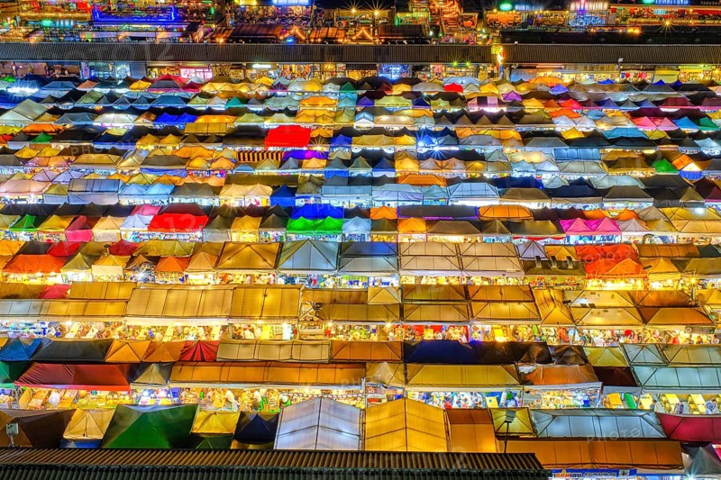 Close-up view of rows of colorful outdoor market tents and food stalls at night. Fairs