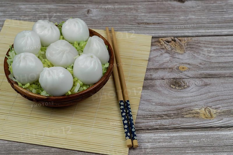 Xiao long bao of prawns on a bed of lettuce in a wooden bowl with chopsticks and a ceramic spoon with soy sauce