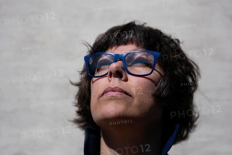 Headshot on a Elegant Woman with Eyeglasses and Looking Up and Leaning on a Concrete Wall in a Sunny Day in Switzerland
