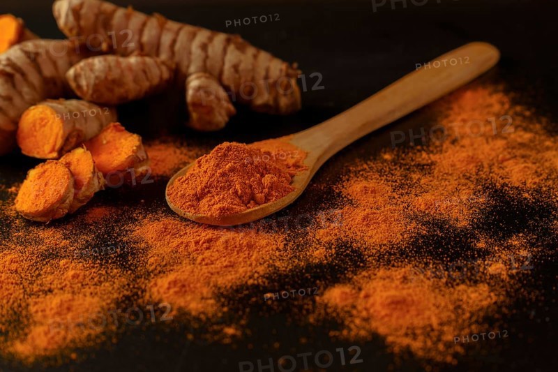 Fresh turmeric root and ground turmeric in a wooden spoon isolated on black background and copy space