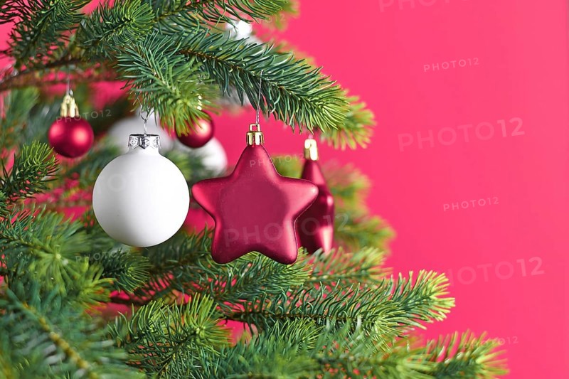 Close up of decorated Christmas tree with pink star shaped and white ball shaped tree ornament baubles on pink background