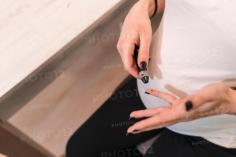Young pregnant woman performing a gestational diabetes self-test to control sugar. Bleeding blood from his finger with a prick