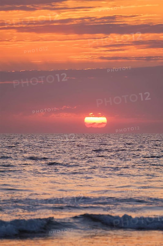 Ocean waves on sunset with setting sun background