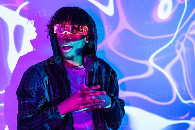 Studio portrait with purple and blue neon lights of an amazed futuristic afro man wearing an augmented reality goggles