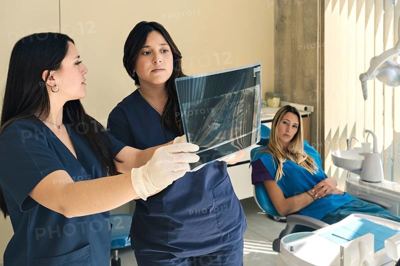Dentist and assistant holding an x-ray and patient watching sitting in dental office chair