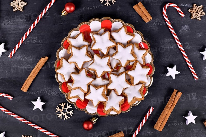 German star shaped glazed cinnamon Christmas cookies called 'Zimtsterne' on striped plate surrounded by cinnamon sticks and seasonal decoration