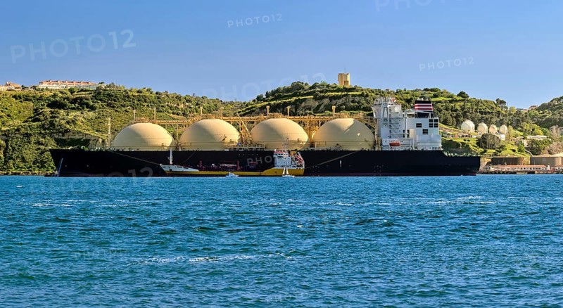 LNG or liquified natural gas tanker moored by industrial pier and green hill on sunny day. Alternative gas supply