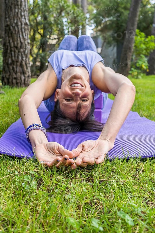 Happy smiling woman lying on yoga blocks while looking at camera. Vertical shot