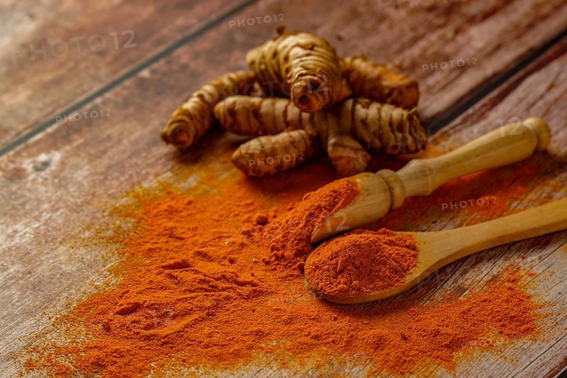 Fresh turmeric root and ground turmeric in a wooden spoon poured out on a wooden table