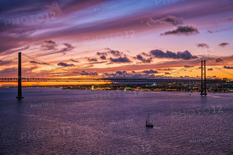 View of 25 de Abril Bridge famous tourist landmark of Lisbon connecting Lisboa and Almada on Setubal Peninsula over Tagus river in the evening twilight with boats. Lisbon