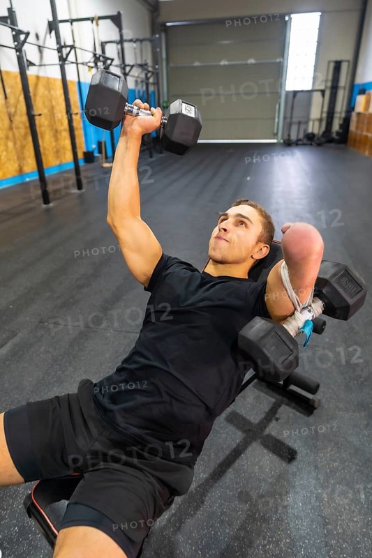 Vertical photo of a strong disabled man exercising with dumbbells in a bench