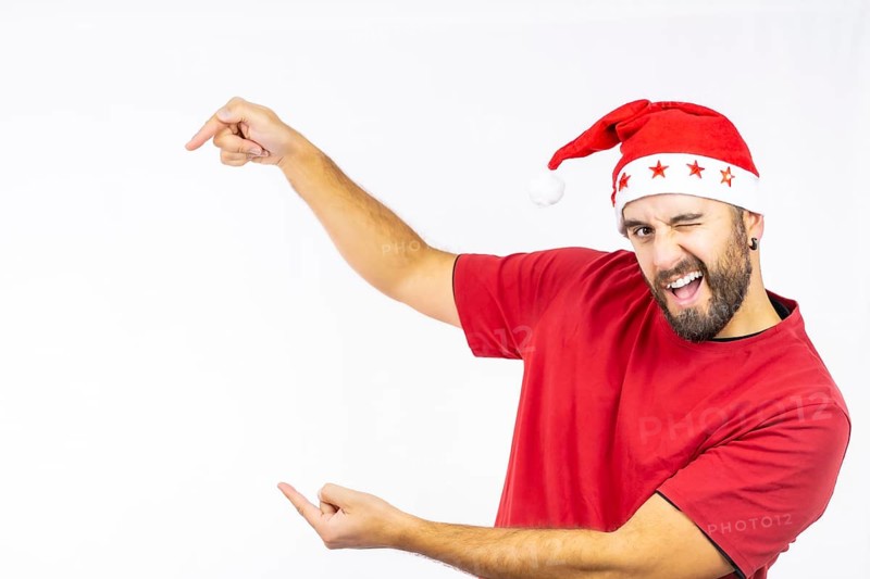 Young very happy Caucasian man with red Christmas hat pointing to the left on a white background