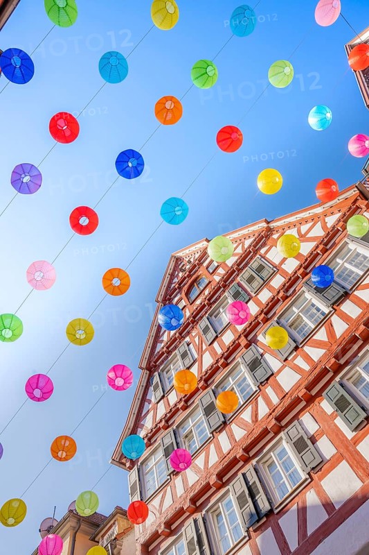 Colourful lanterns hanging in alleyway alley between half-timbered houses