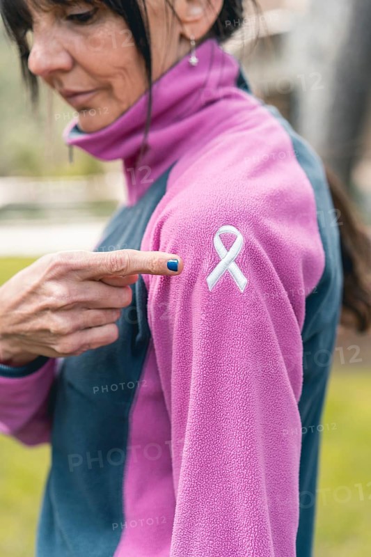 Mid adult woman pointing to an embroidered cancer awareness ribbon with her finger on her sweatshirt. Vertical shot