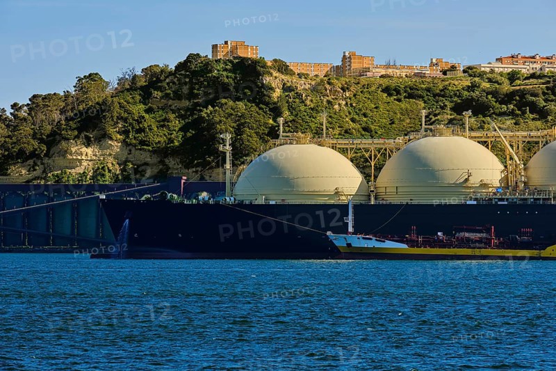 LNG or liquified natural gas tanker moored by industrial pier and green hill on sunny day. Alternative gas supply