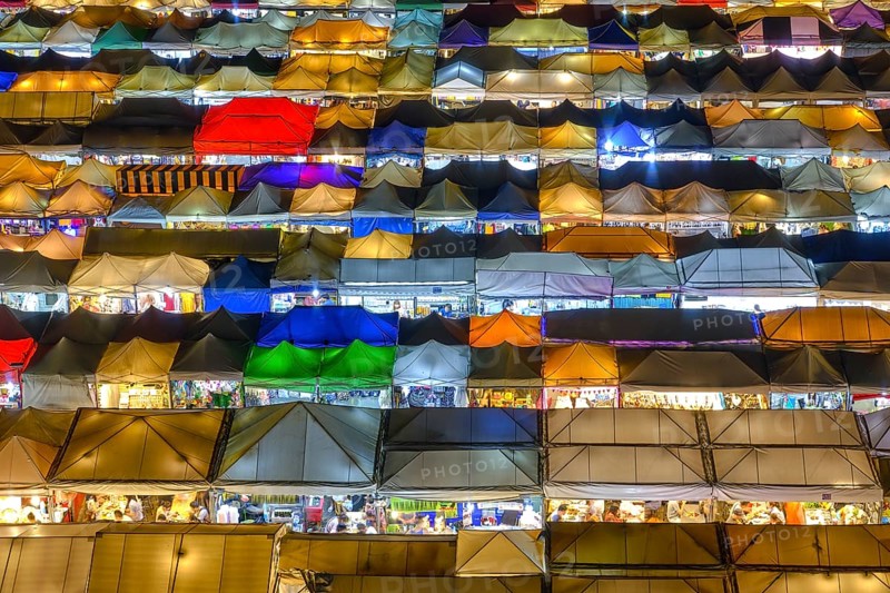 Close-up view of rows of colorful outdoor market tents and food stalls at night. Fairs