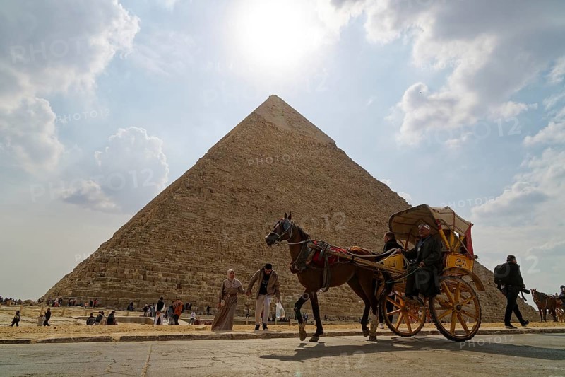 Two-wheeled horse-drawn carriage passes in front of a pyramid