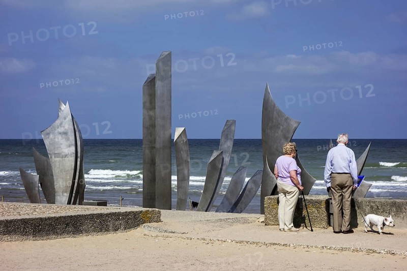 Elderly couple looking at Second World War Two Omaha Beach monument Les Braves at Saint-Laurent-sur-Mer
