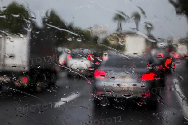Trucks overtaking cars on highway during heavy rain shower seen from inside of vehicle with big raindrops on windscreen