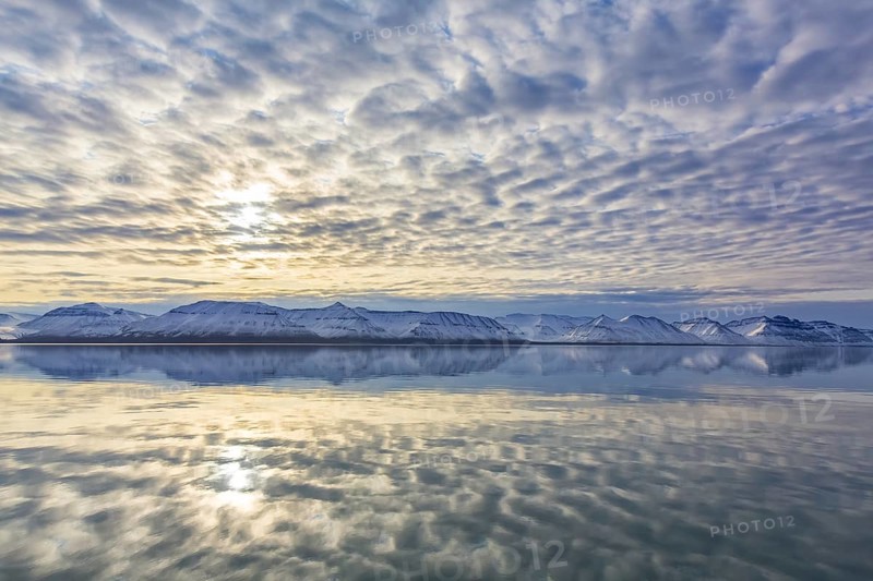 Snow covered mountains at Billefjorden at sunset and clouds reflected in the Arctic sea