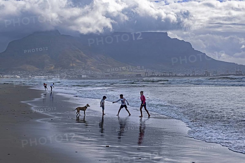 Rain clouds over Table Mountain and children playing on sandy Sunset Beach near Cape Town